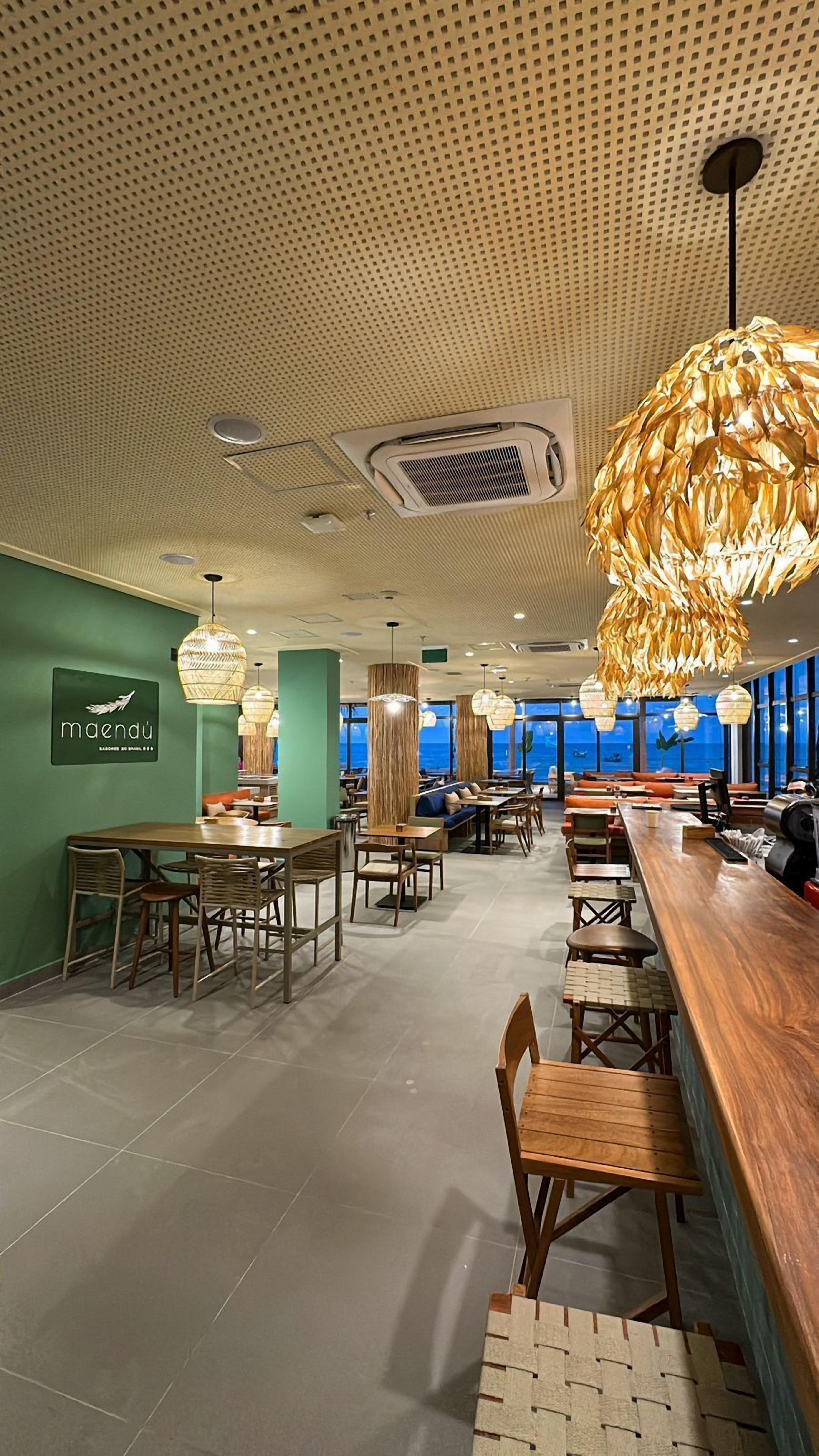 A restaurant interior with a high ceiling, patterned ceiling, and large windows.
