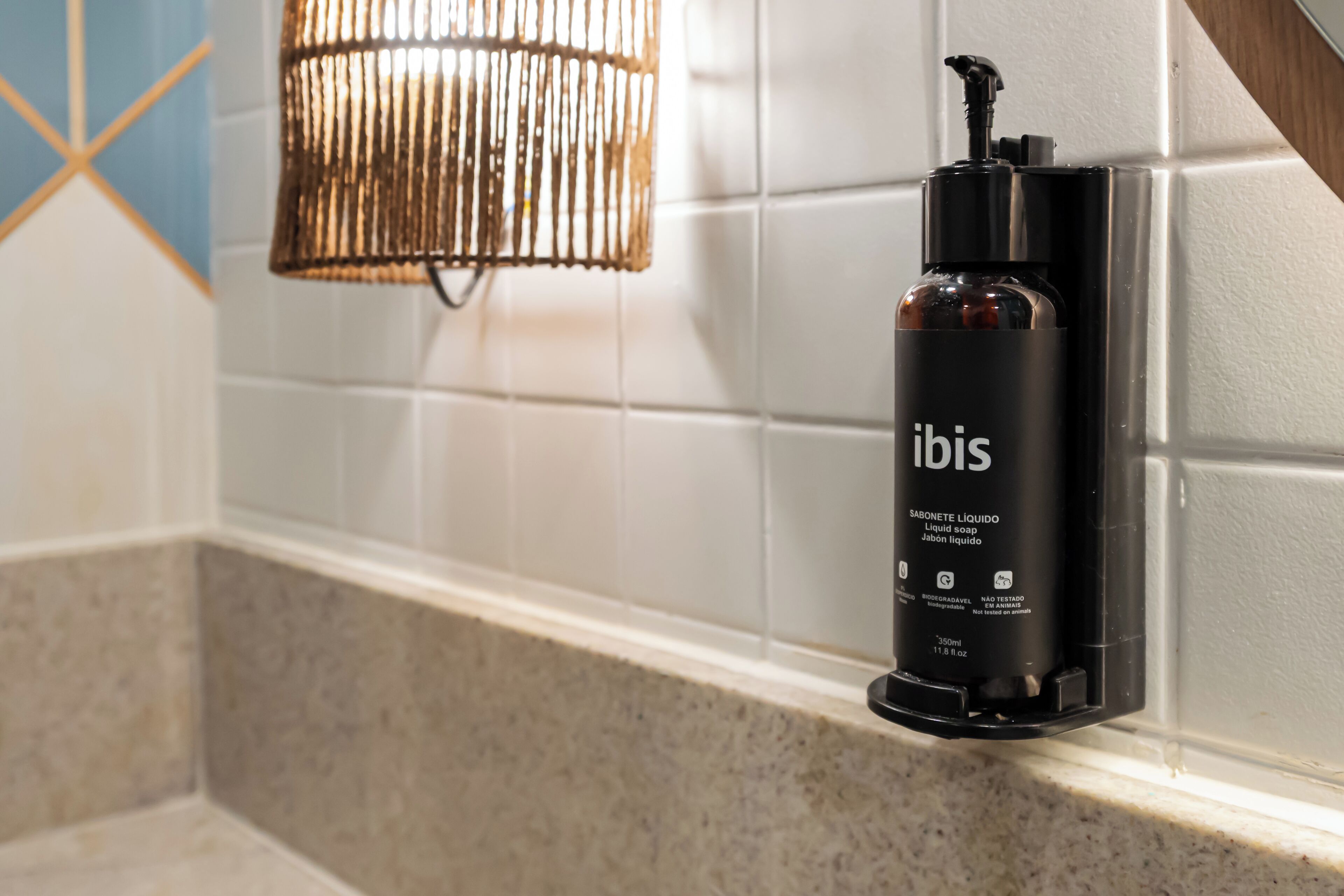 En svart flaska med flytande tvål, märkt med texten ”ibis”, står på en hylla i badrummet.