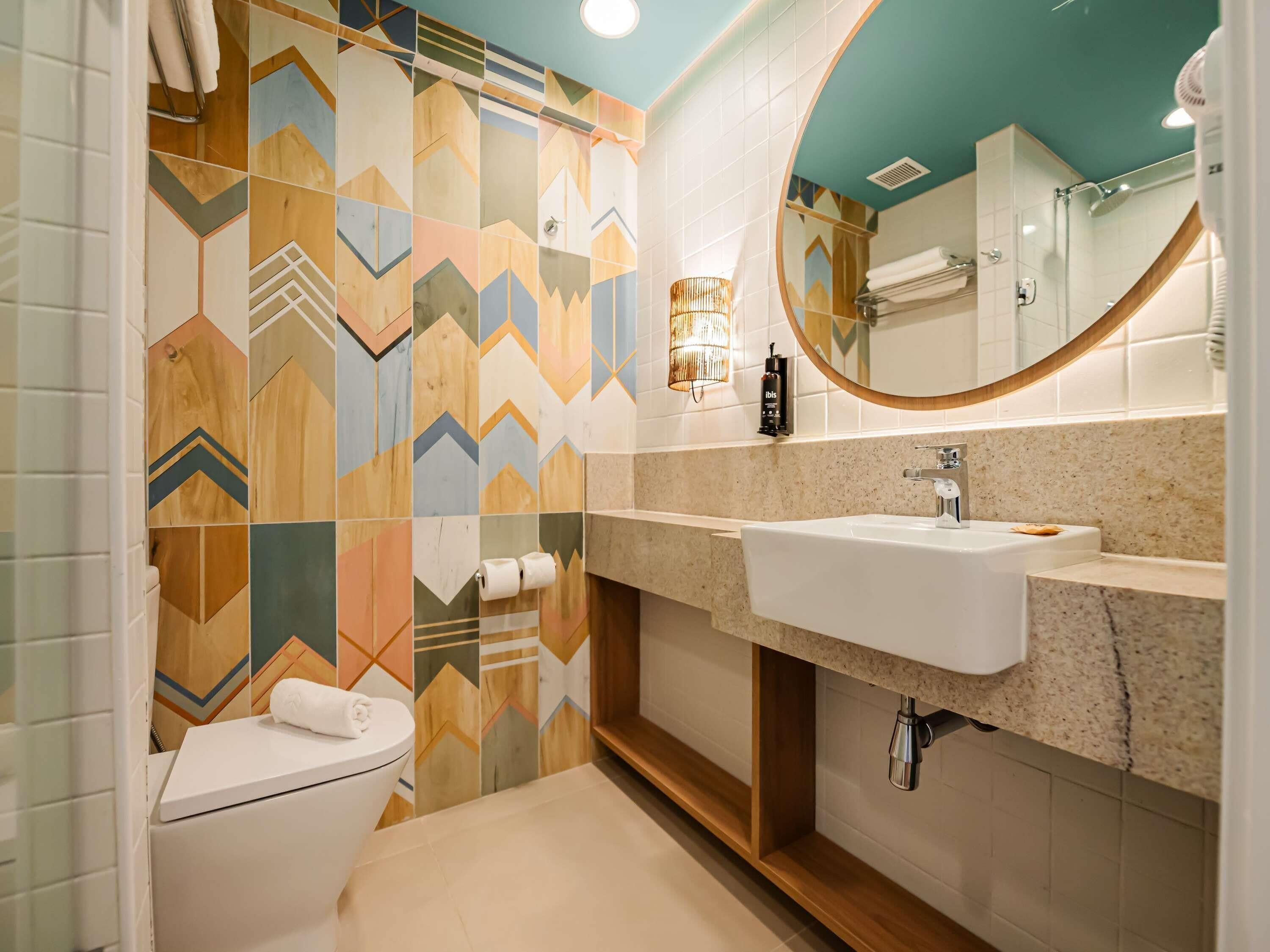 Un baño moderno con un salpicadero de azulejos geométricos, un lavabo blanco y un espejo redondo.