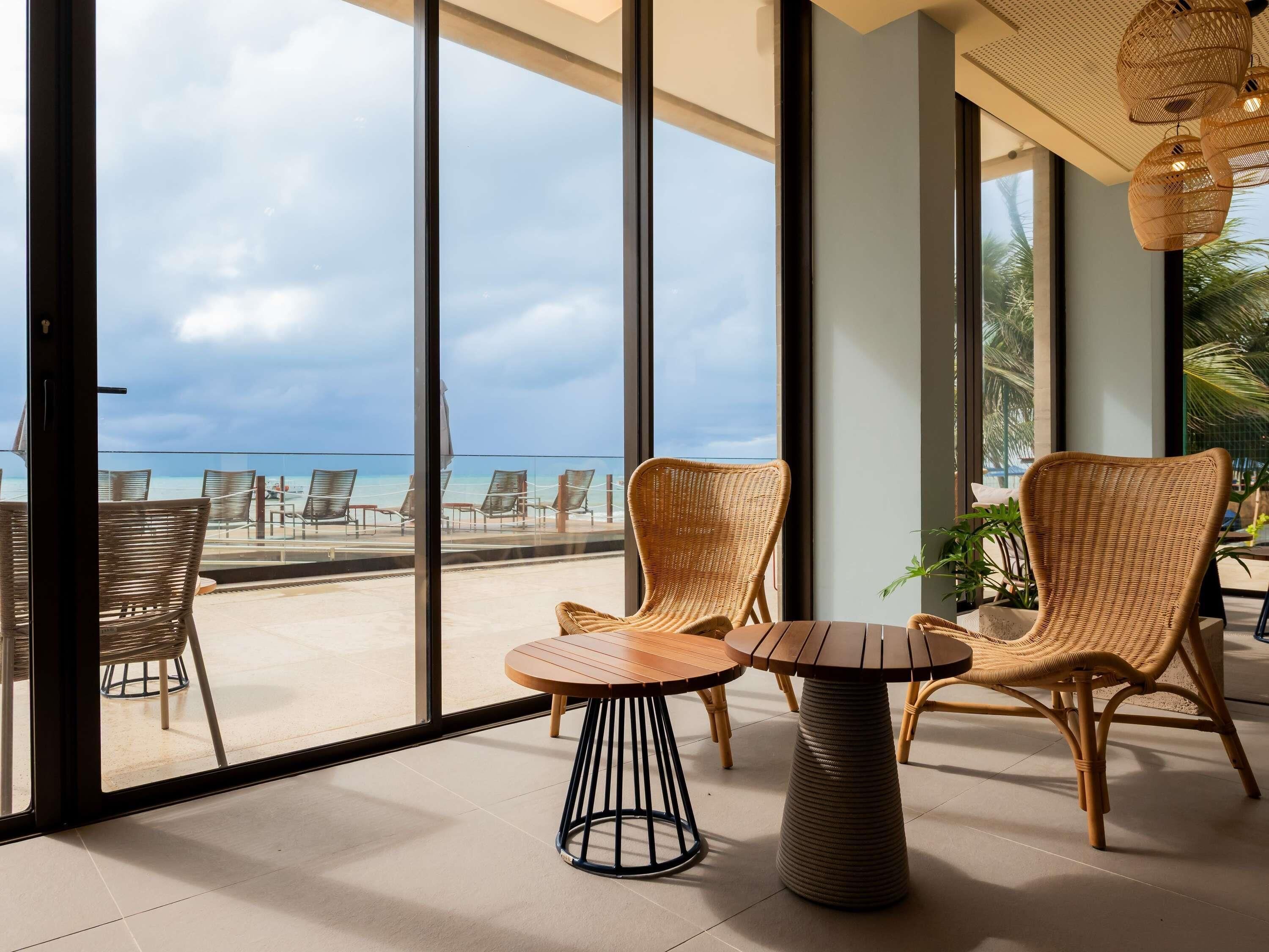 Quarto com janelas amplas, mobiliário de vime e vista para a praia.