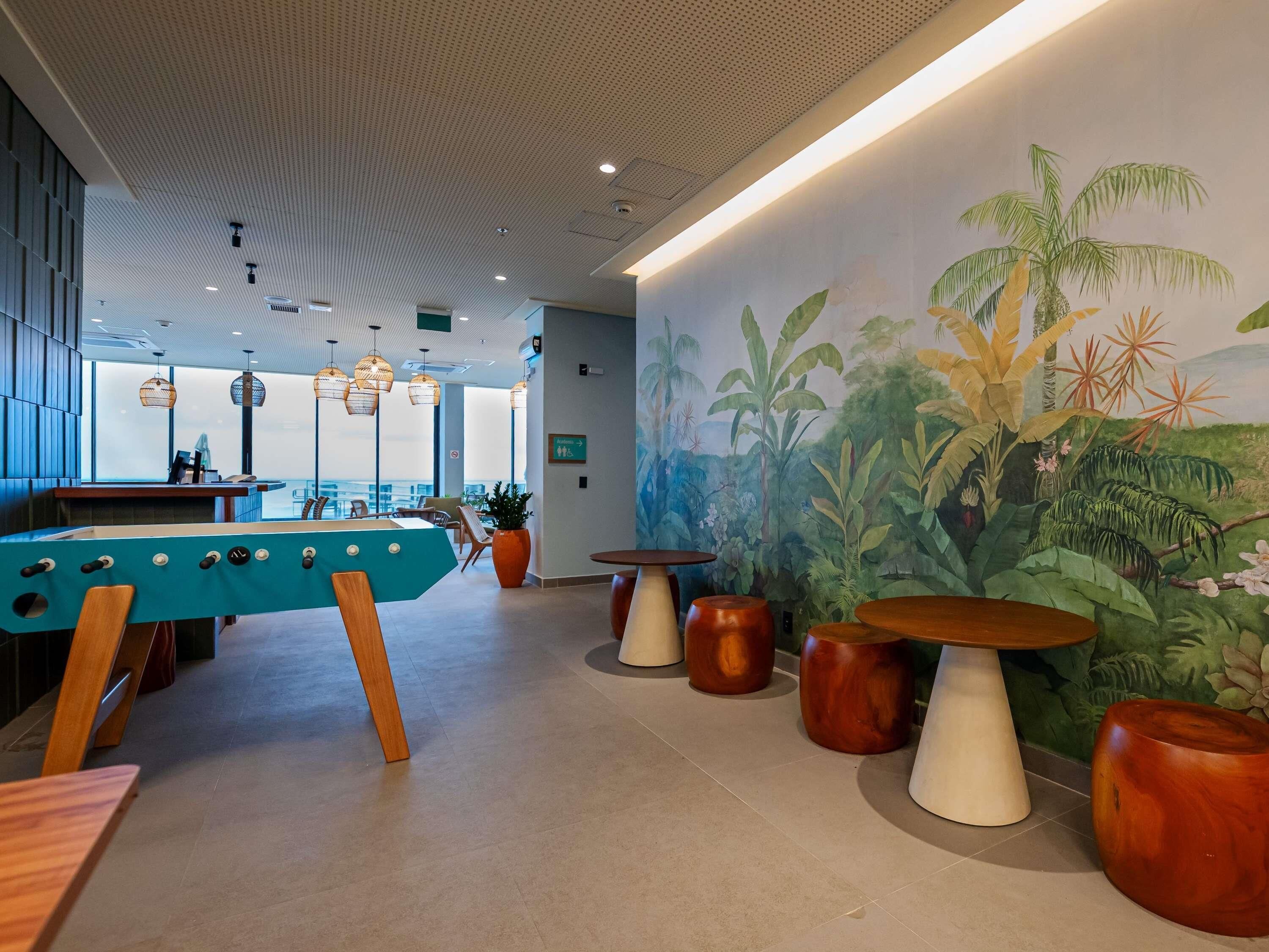 Un área de descanso moderna con mesa de billar, asientos y un mural de plantas tropicales.
