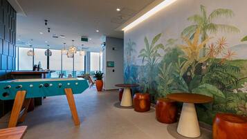Un área de descanso moderna con mesa de billar, asientos y un mural de plantas tropicales.