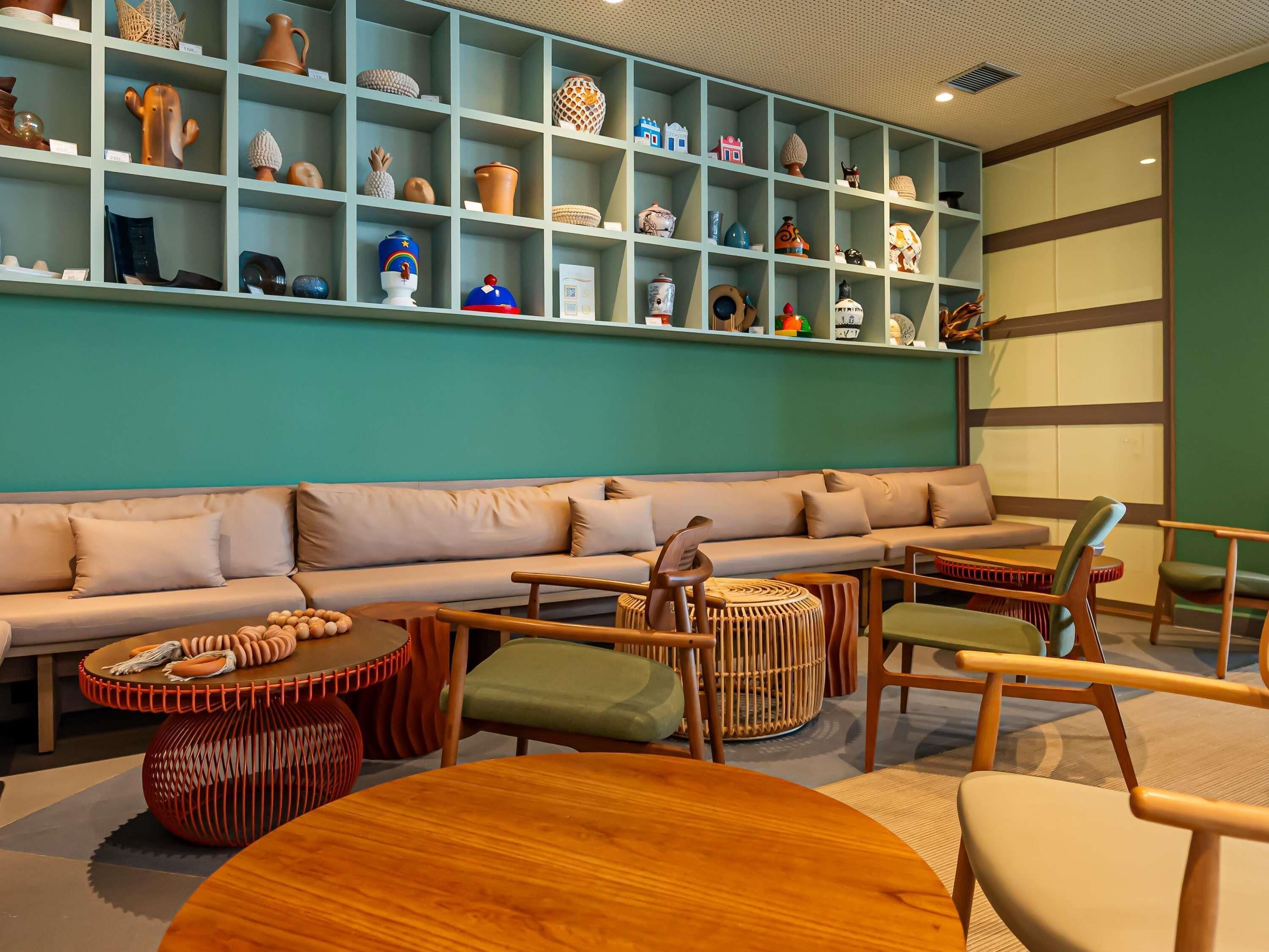 A modern interior with a teal-colored wall, a beige sofa, wooden furniture, and a display of various pottery and decorative items.