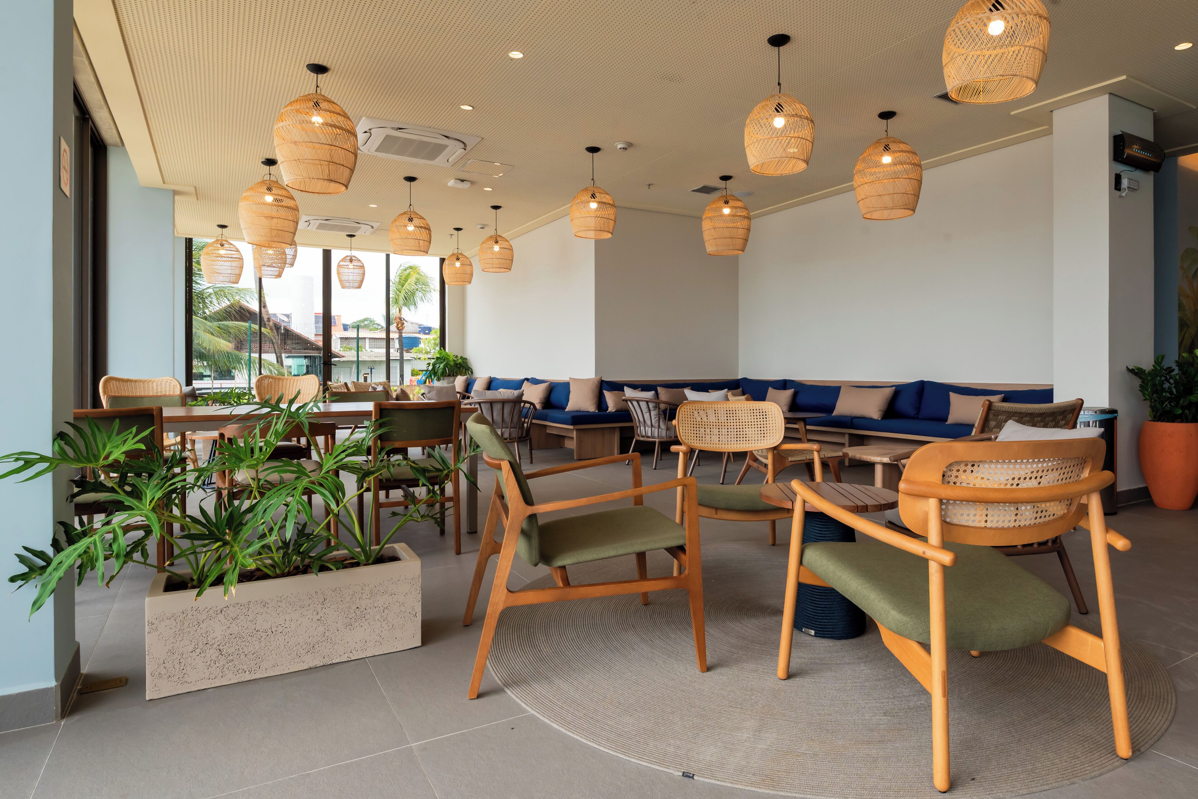 A modern interior with wicker pendant lighting, a seating area with sofas and chairs, and potted plants.