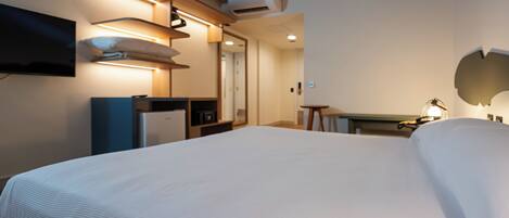 A hotel room with a large bed, a desk, a television mounted on the wall, and a ceiling-mounted air conditioning unit.