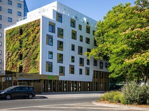 Un hotel moderno con facciata bianca, ampie finestre e un giardino verticale verde.