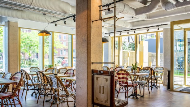 A spacious indoor dining area with high ceilings, exposed ductwork, and large windows offering views of the outside. - ibis Styles Paris Porte de Pantin Philharmonie (Pantin)