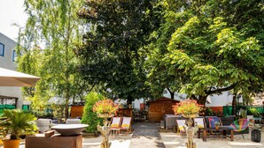 An outdoor seating area with tables and chairs, surrounded by lush greenery and trees. - ibis Styles Paris Porte de Pantin Philharmonie (Pantin)
