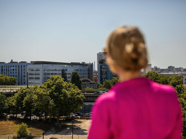 A woman in a pink shirt overlooking a cityscape with modern buildings and trees. - ibis Styles Paris Porte de Pantin Philharmonie (Pantin)