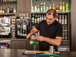 A bartender preparing a drink at a bar with shelves of liquor bottles in the background. - ibis Styles Paris Porte de Pantin Philharmonie (Pantin)