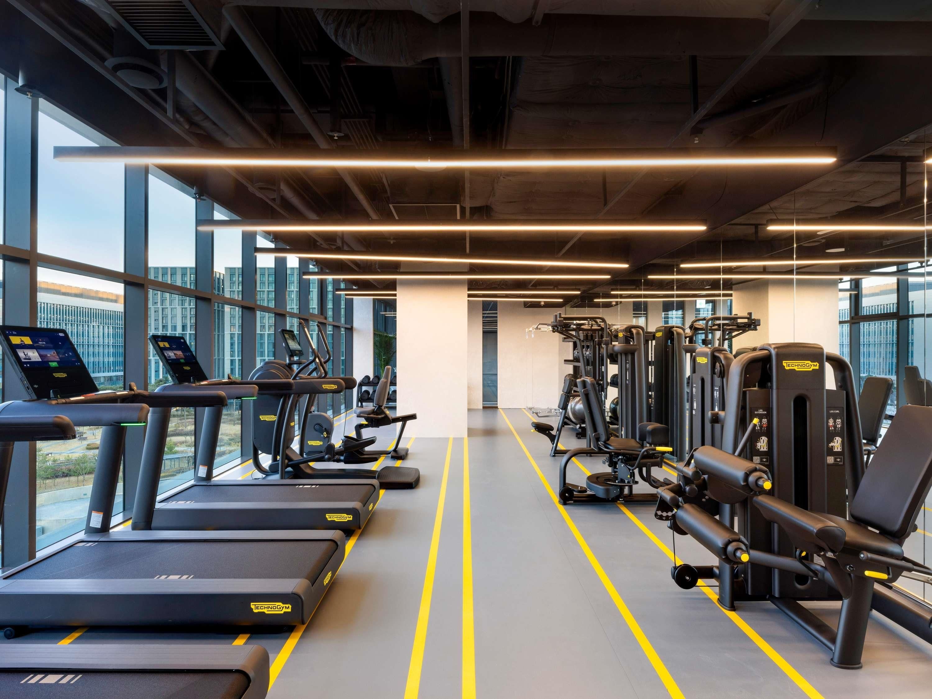 A gym with treadmills, weight machines, and a clear view of the outside through large windows.
