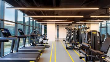 A gym with treadmills, weight machines, and a clear view of the outside through large windows.