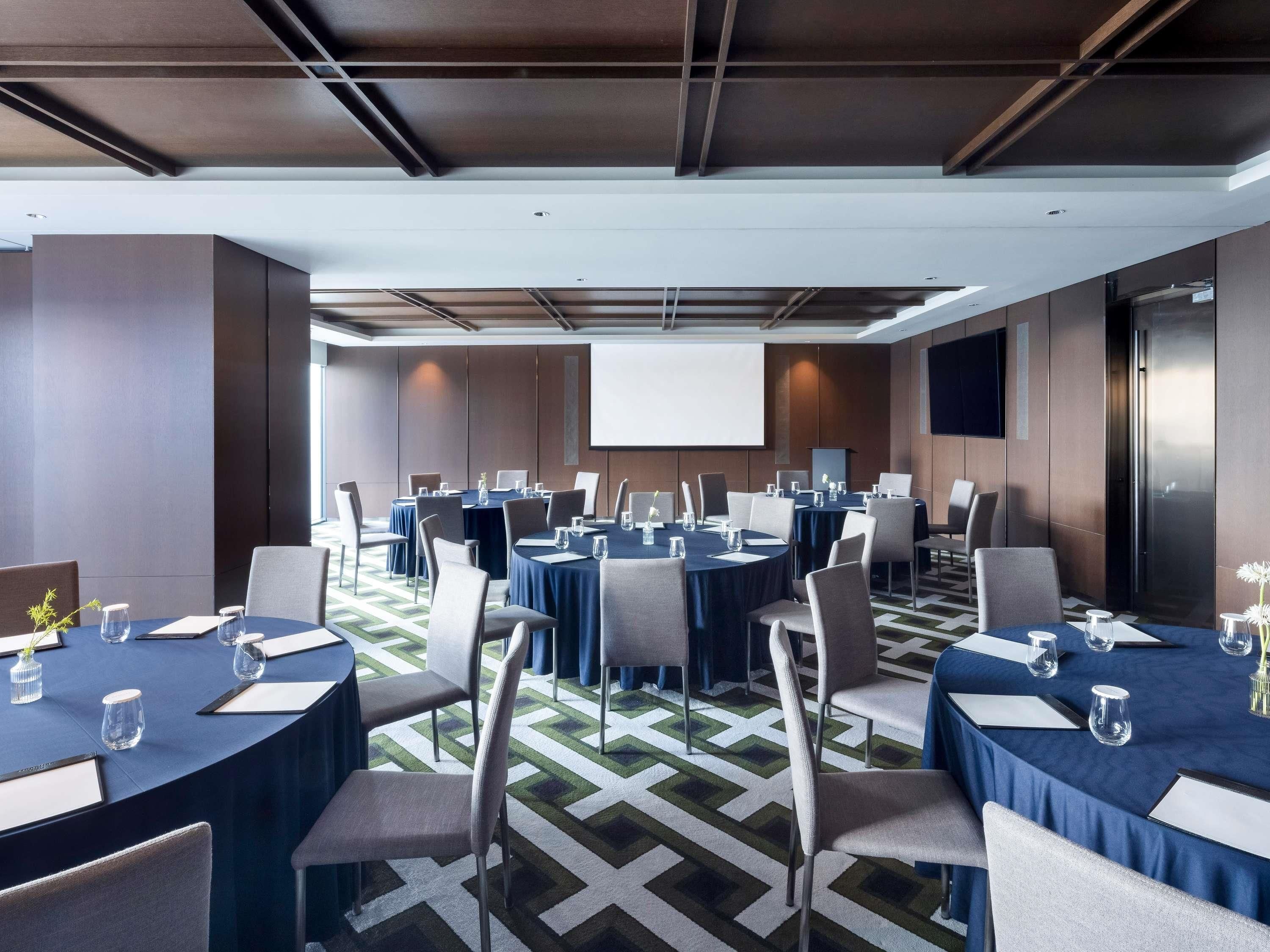 A conference room with multiple tables, chairs, and a projector screen.
