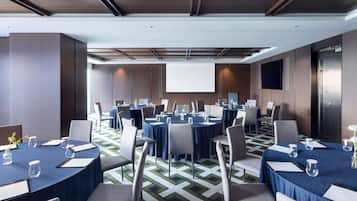A conference room with multiple tables, chairs, and a projector screen.