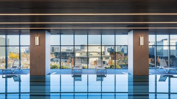 Une piscine intérieure moderne avec des parois en verre transparent, des chaises longues et une vue sur le paysage urbain.