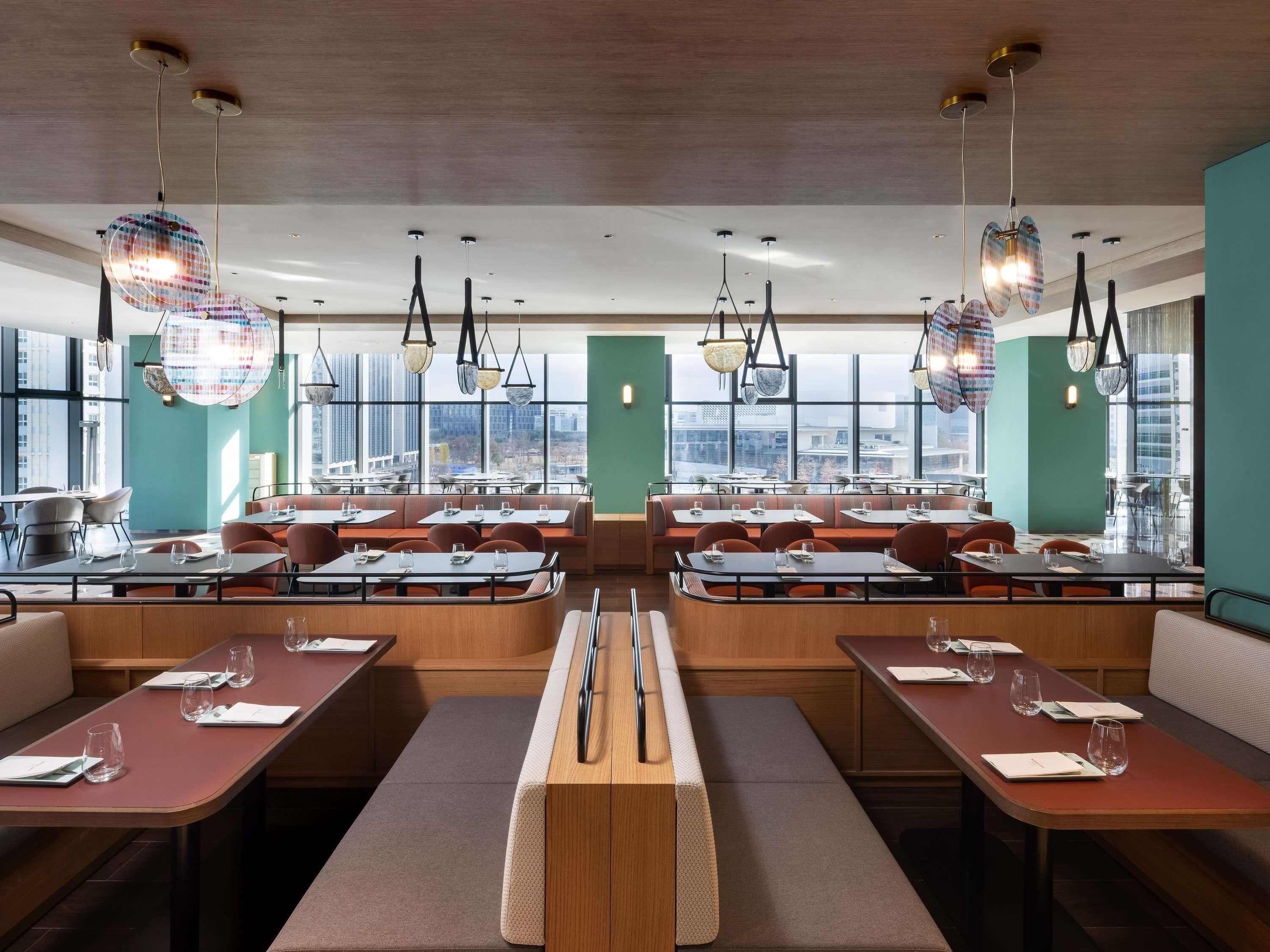 A modern restaurant with high tables and booths, large windows, and city views.