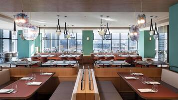 A modern restaurant with high tables and booths, large windows, and city views.