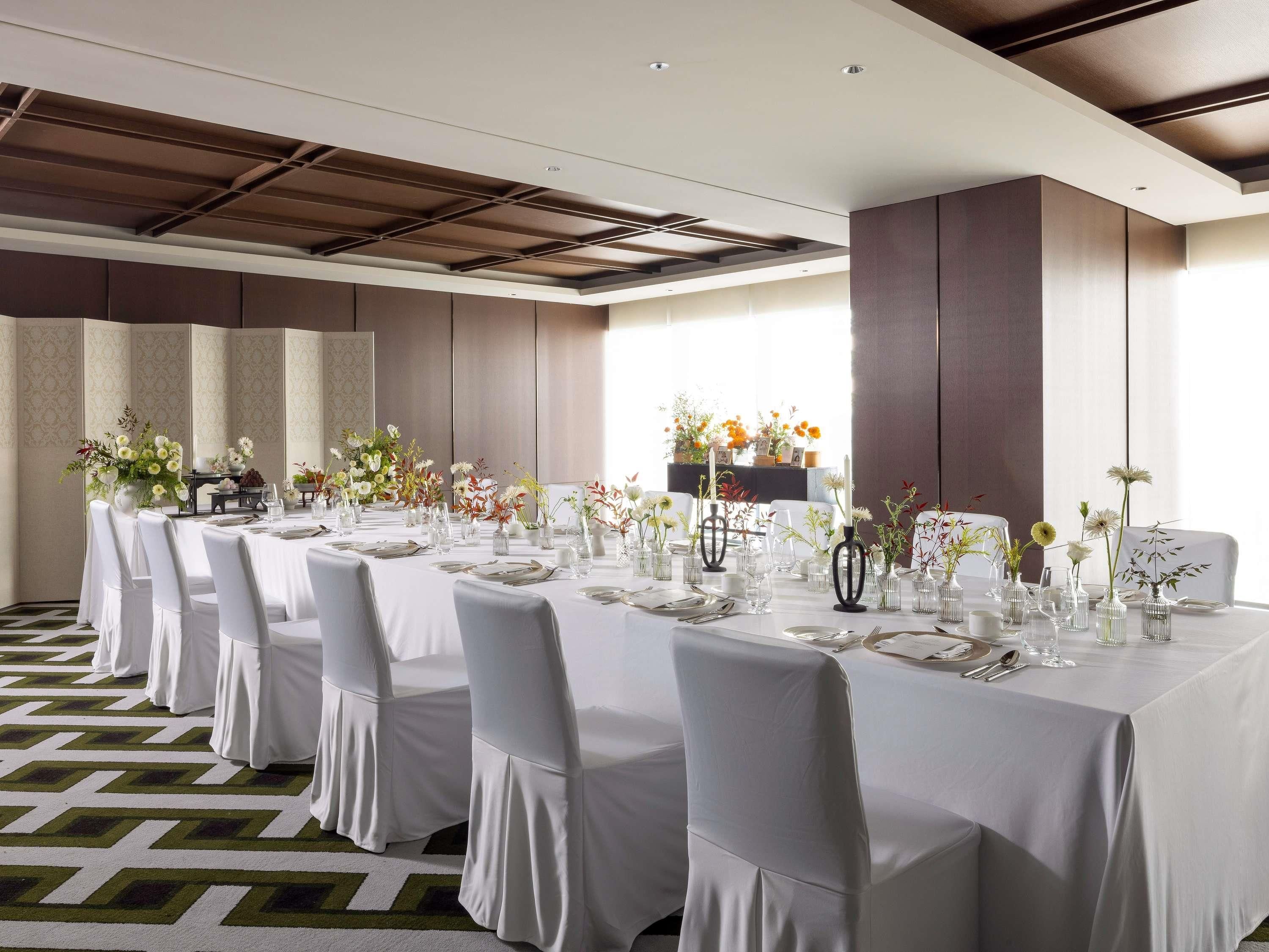 A long dining table with white tablecloths and chairs, set with glassware and floral centerpieces.