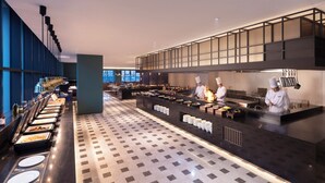 Une cuisine d’hôtel moderne, avec un service de type buffet, des chefs en pleine activité et un long comptoir où sont présentés les plats.