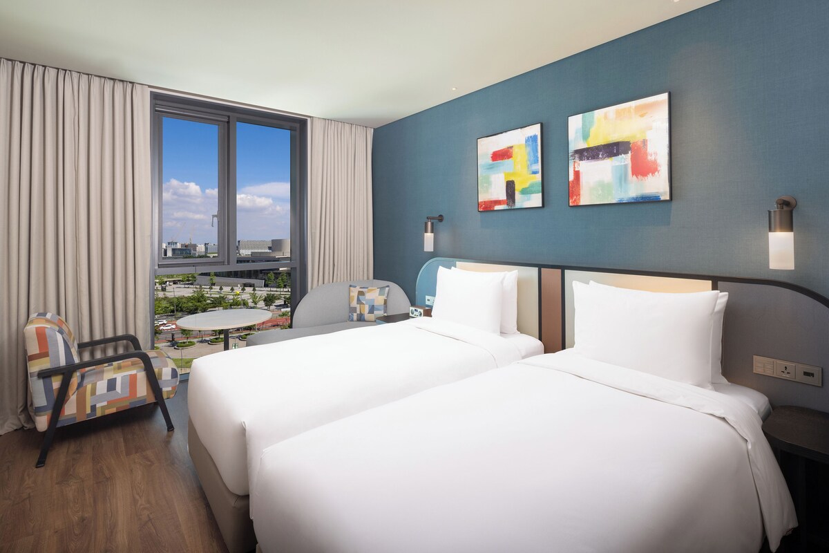 Habitación de hotel con dos camas, vistas a la ciudad, una mesa de comedor y una silla.