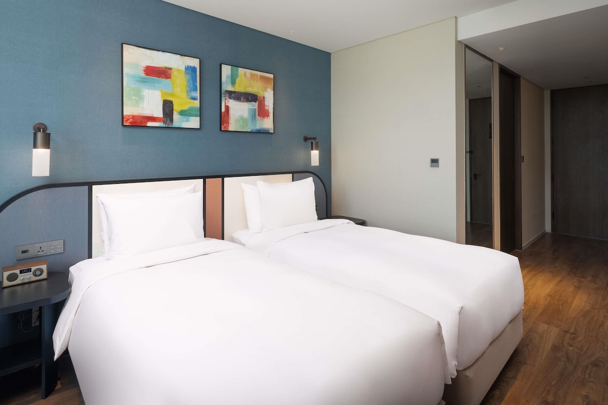 A hotel room with a large bed, two wall-mounted light fixtures, and two abstract paintings.