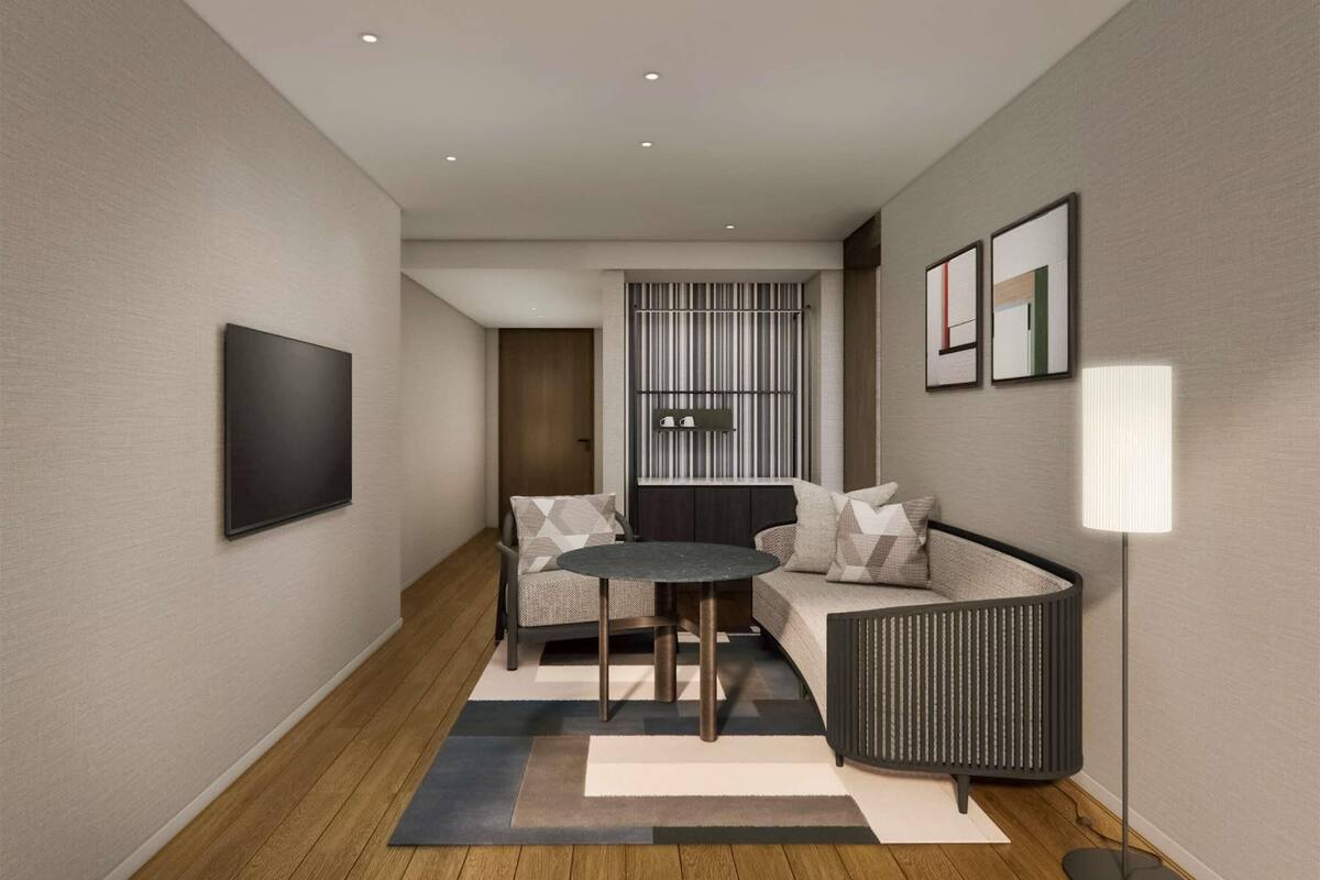 A modern hotel room with a sofa, a small round table, a floor lamp, and a TV mounted on the wall.