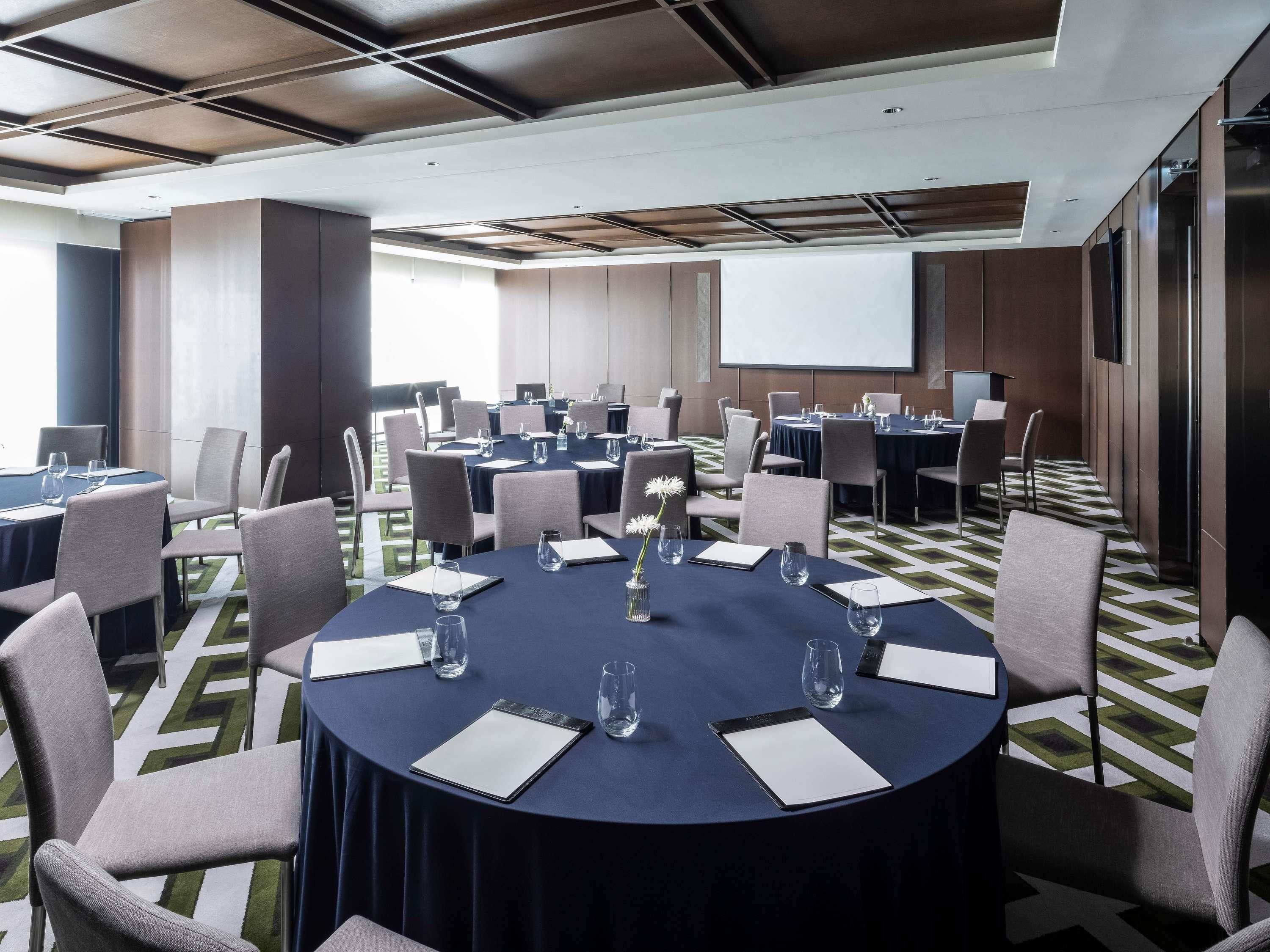A conference room with round tables, chairs, and a projector screen.