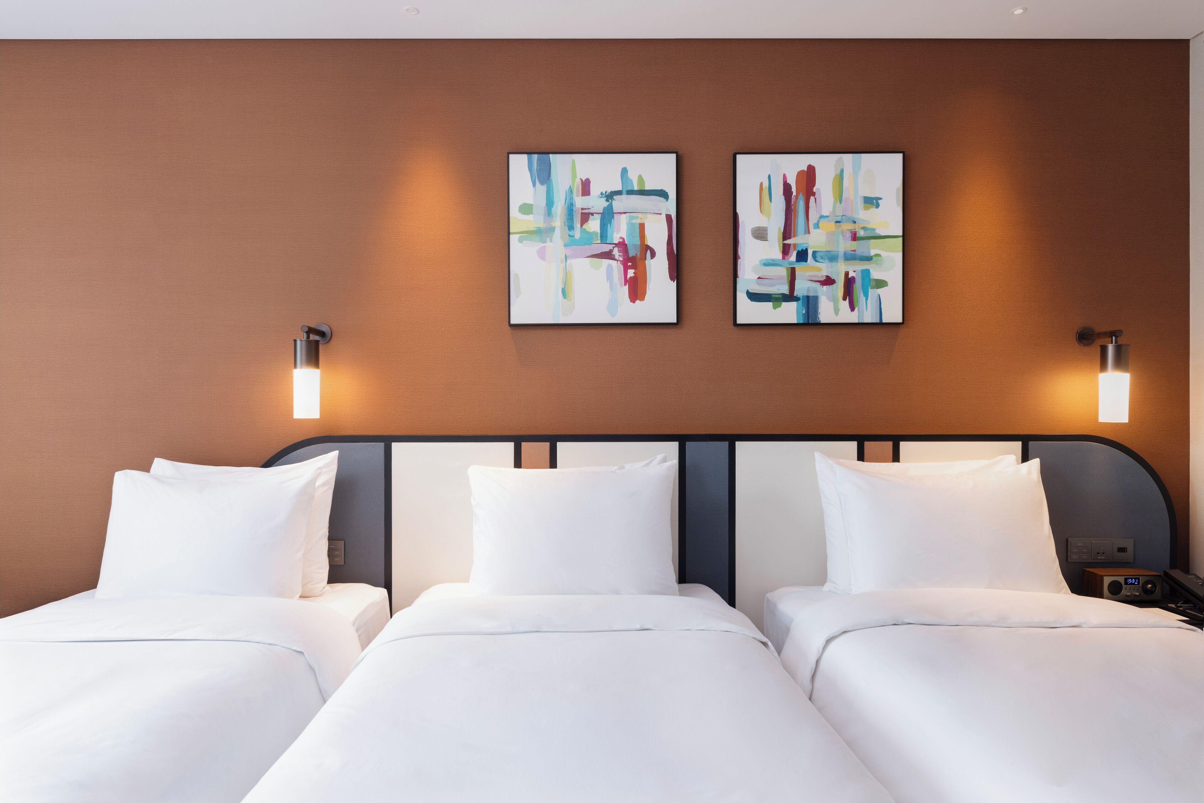 A hotel room with two beds, white bedding, and abstract art on the wall.