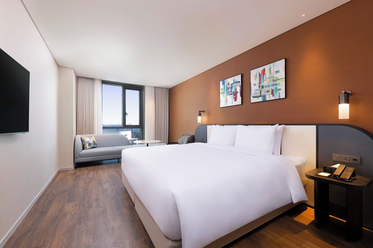 Una habitación de hotel moderna con una cama grande, un sofá, un escritorio y una ventana con cortinas.