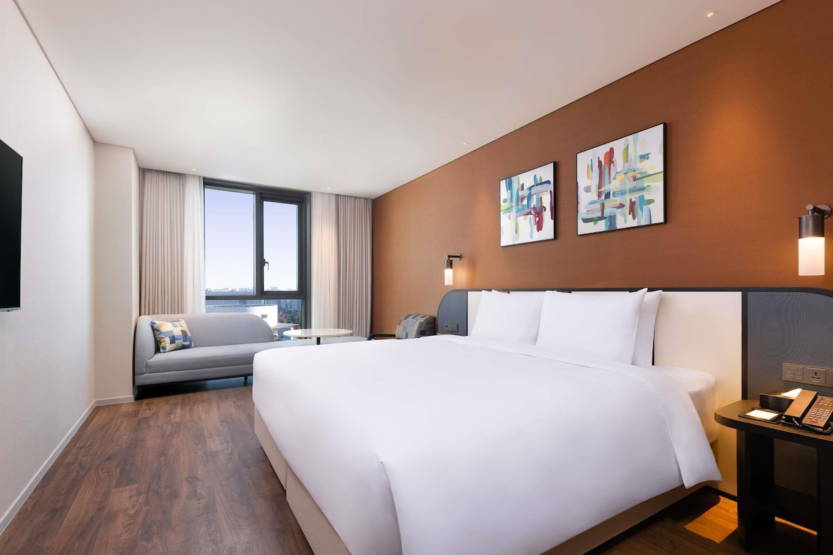 A modern hotel room with a large bed, a sofa, a small table, and artwork on the walls.