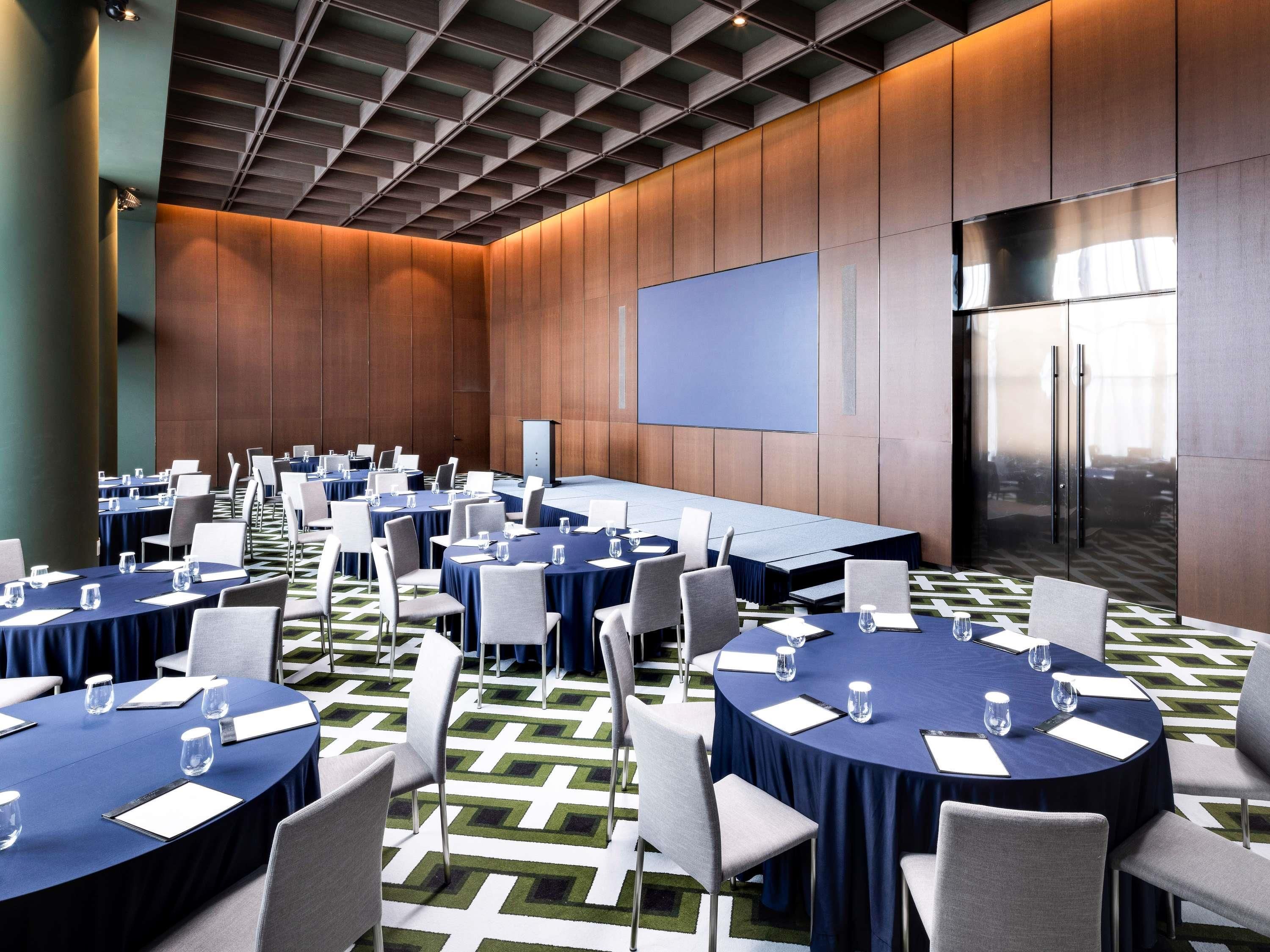 Un salón de conferencias con varias mesas, sillas y una pantalla grande.