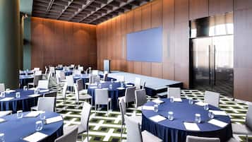 Un salón de conferencias con varias mesas, sillas y una pantalla grande.