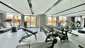 A modern gym with various exercise equipment, large windows, and a view of the outside. - Waves - Ideal Dubai Retreat Elegant St (Dubai)