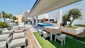 A rooftop terrace with a swimming pool, outdoor seating, and a view of the city skyline. - Waves - Ideal Dubai Retreat Elegant St (Dubai)