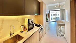 A modern kitchen with a sink, stove, and microwave. There is a dining area with a table and chairs. The room has a large window with a view of buildings outside. - Waves - Ideal Dubai Retreat Elegant St (Dubai)