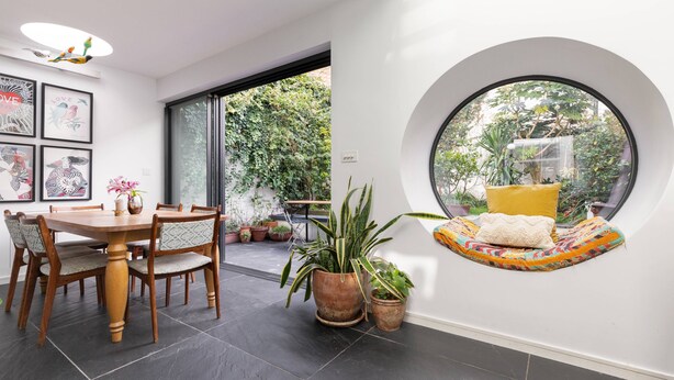 A dining area with a round table and chairs, surrounded by potted plants and framed artwork on the walls. - Colville Terrace IV by Onefinestay (London)