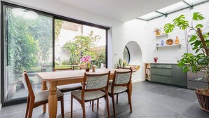 A modern kitchen with a large island, a dining area with a wooden table and chairs, and a view of a garden through large windows. - Colville Terrace IV by Onefinestay (London)