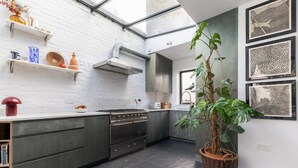 A modern kitchen with dark cabinetry, a stainless steel range hood, and a large window. - Colville Terrace IV by Onefinestay (London)