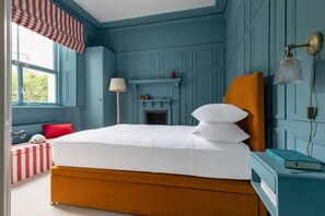 Une chambre avec un grand lit, une petite table de chevet, un banc à rayures rouges et blanches et une cheminée.