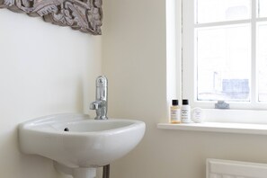 Une salle de bain avec un lavabo blanc, un miroir et une fenêtre. Deux flacons de lotion sont posés sur le rebord de la fenêtre.