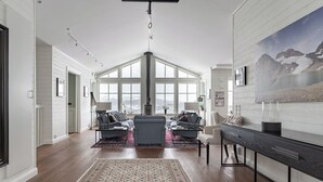 A spacious living room with a high ceiling, large windows, a fireplace, and a modern console table. - Amazing ski in/ski out Chalet in Åre - Övre Sadelvägen Ski Lodge   (Jämtlands län)