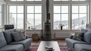 A cozy living room with a large fireplace, grey sofas, and a view of a snowy landscape through large windows. - Amazing ski in/ski out Chalet in Åre - Övre Sadelvägen Ski Lodge   (Jämtlands län)