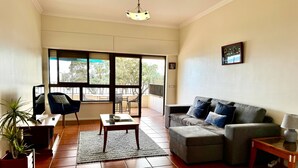 A living room with a sofa, a coffee table, a chair, a TV, and a plant.