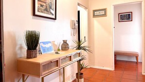 A hallway with a wooden console table, potted plants, framed artwork, and a bench.