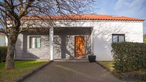 Una casa moderna con un camino de ladrillo que lleva a una puerta de madera, una ventana con cortinas y una planta en maceta a su lado.