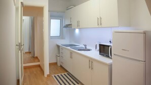 A modern kitchen with white cabinets, a sink, a microwave, and a refrigerator. - CASA DO COLÉGIO 57 by Azores HomeMade (Ponta Delgada)
