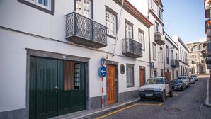 A narrow cobblestone street lined with white buildings, featuring green doors and balconies. - CASA DO COLÉGIO 57 by Azores HomeMade (Ponta Delgada)