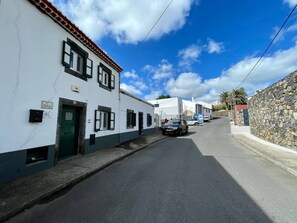 A narrow street with white buildings, a stone wall on one side, and a clear blue sky. - CASA O REFÚGIO by Azores HomeMade (Lagoa (Açores))