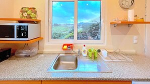 Eine Küche mit Fensterblick, einer Mikrowelle, einem Brotkasten und einem Spülbecken.