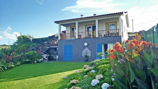 Ein zweistöckiges Haus mit Balkon, gepflegtem Rasen und bunten Blumen.